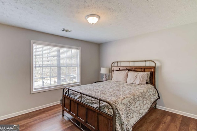 bedroom with baseboards, visible vents, dark wood finished floors, and a textured ceiling