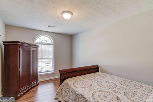 bedroom featuring baseboards, a textured ceiling, visible vents, and wood finished floors