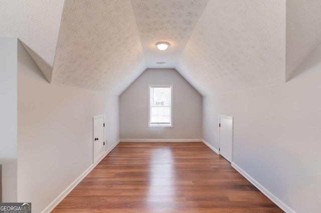 bonus room featuring lofted ceiling, dark wood-type flooring, a textured ceiling, and baseboards