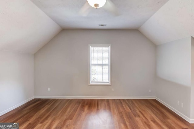 additional living space featuring baseboards, visible vents, lofted ceiling, wood finished floors, and a textured ceiling