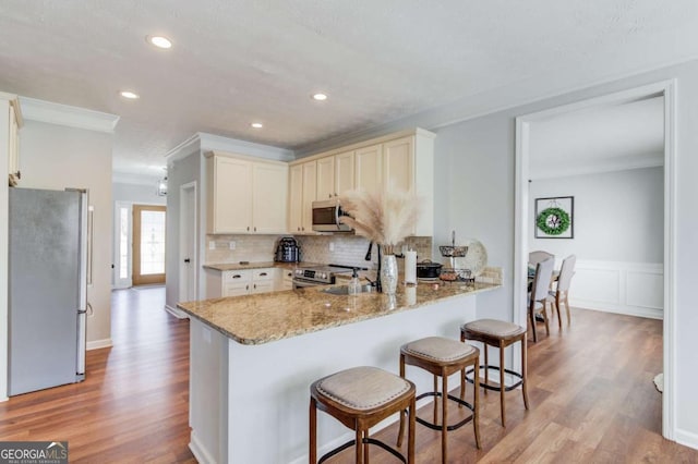 kitchen featuring light stone counters, a peninsula, a kitchen breakfast bar, appliances with stainless steel finishes, and crown molding