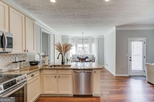 kitchen with appliances with stainless steel finishes, a sink, a peninsula, and light stone countertops