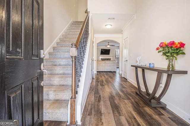 entryway with arched walkways, a fireplace, dark wood finished floors, baseboards, and stairs