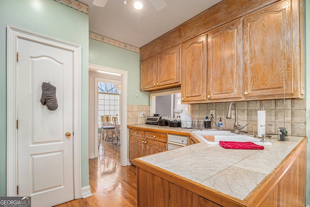 kitchen featuring a peninsula, a sink, tile counters, and brown cabinets