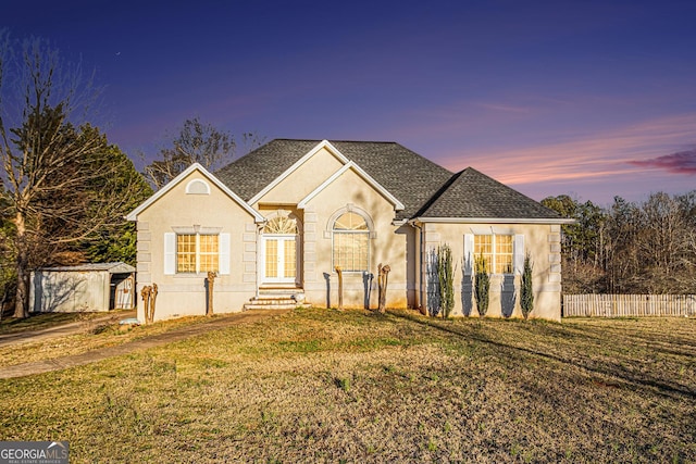 view of front of home featuring an outbuilding, a shingled roof, a lawn, stucco siding, and a shed