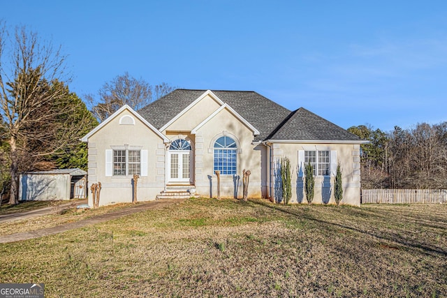 view of front of property featuring a front lawn, a shingled roof, an outdoor structure, and stucco siding