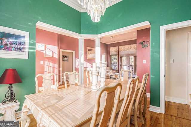 dining space with a notable chandelier, crown molding, ornate columns, wood finished floors, and baseboards