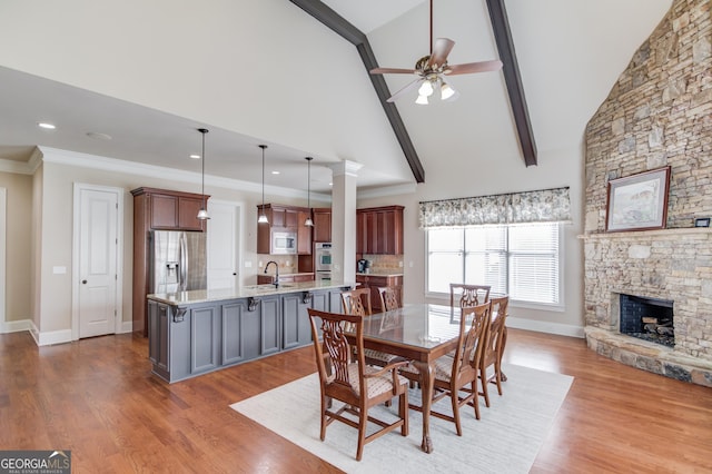 dining space with a ceiling fan, wood finished floors, crown molding, a stone fireplace, and high vaulted ceiling