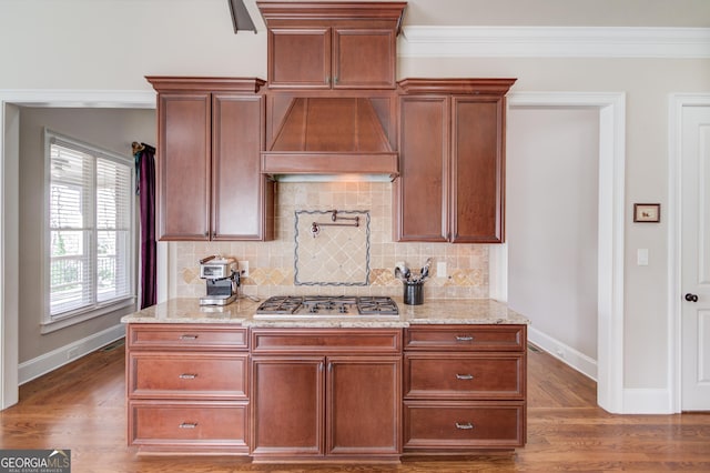 kitchen featuring light stone counters, ornamental molding, wood finished floors, premium range hood, and stainless steel gas cooktop