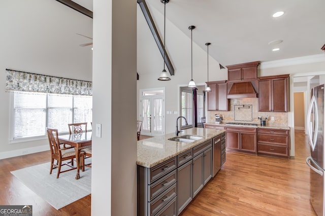 kitchen with decorative backsplash, custom exhaust hood, stainless steel appliances, light wood-style floors, and a sink