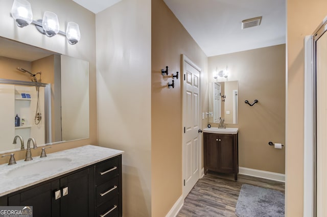 full bath featuring baseboards, visible vents, wood finished floors, a sink, and two vanities