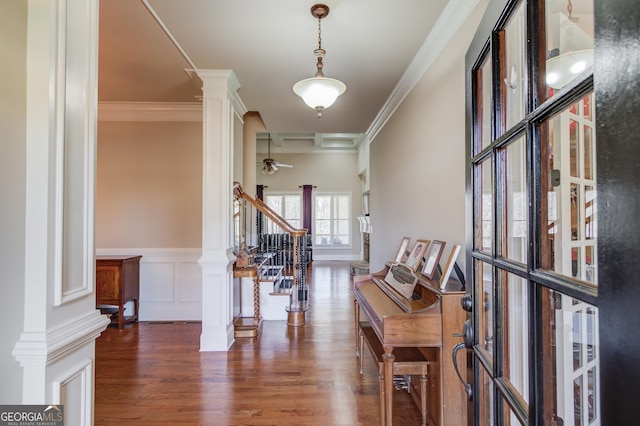 corridor featuring wainscoting, ornamental molding, wood finished floors, stairs, and ornate columns