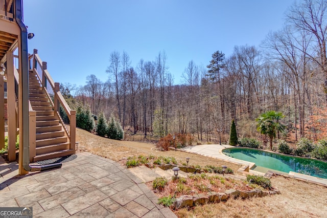 exterior space featuring a patio, stairway, a forest view, and an outdoor pool