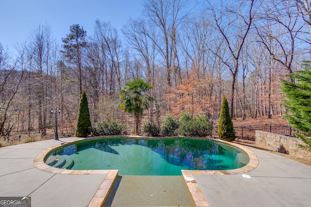 view of swimming pool featuring a fenced in pool, a patio, a forest view, and fence