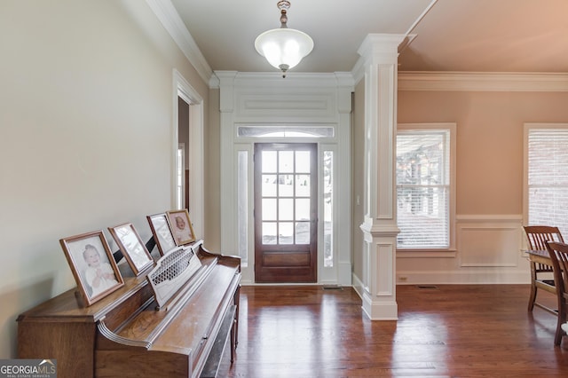 foyer featuring crown molding, a wainscoted wall, dark wood finished floors, and ornate columns