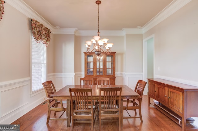 dining area with ornamental molding, light wood-type flooring, a wainscoted wall, and an inviting chandelier