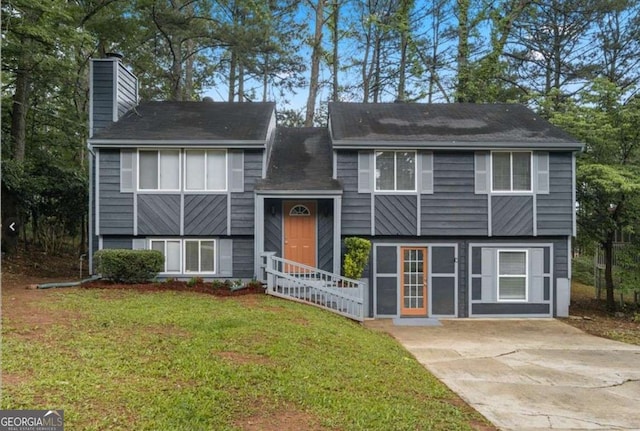 raised ranch featuring a chimney, concrete driveway, and a front yard