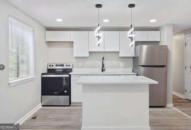 kitchen featuring a kitchen island, a sink, stainless steel appliances, light countertops, and white cabinets