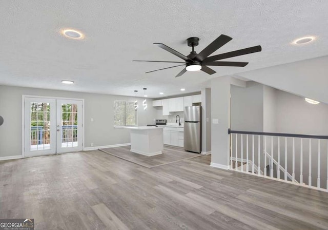 unfurnished living room with light wood-style flooring, french doors, baseboards, and a textured ceiling