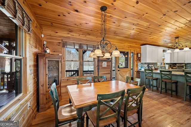 dining space featuring a chandelier, wooden walls, wood ceiling, a wealth of natural light, and light wood finished floors