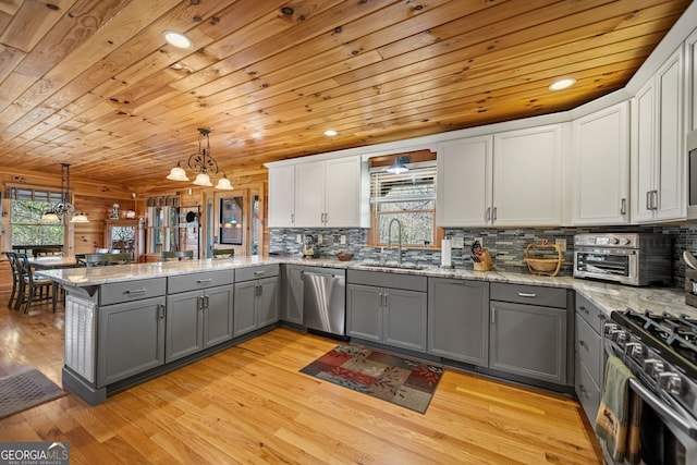 kitchen featuring a peninsula, gray cabinets, stainless steel appliances, and hanging light fixtures