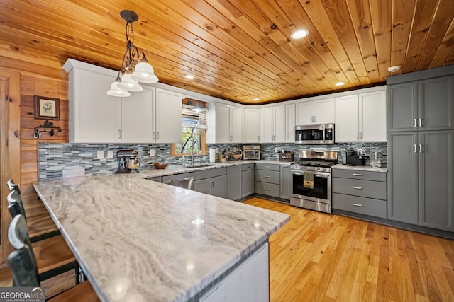 kitchen featuring a peninsula, a sink, appliances with stainless steel finishes, gray cabinets, and pendant lighting