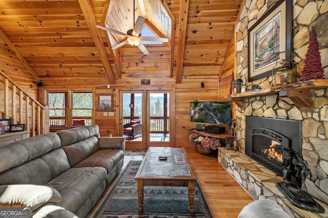 living area with wooden ceiling, wood finished floors, stairs, a stone fireplace, and wood walls