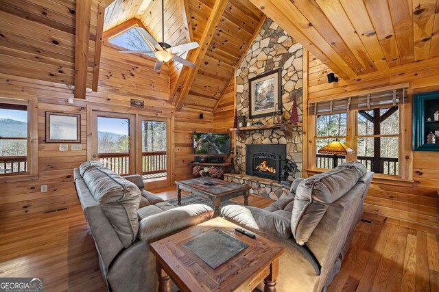 living area featuring wooden ceiling, wood walls, a stone fireplace, and wood finished floors