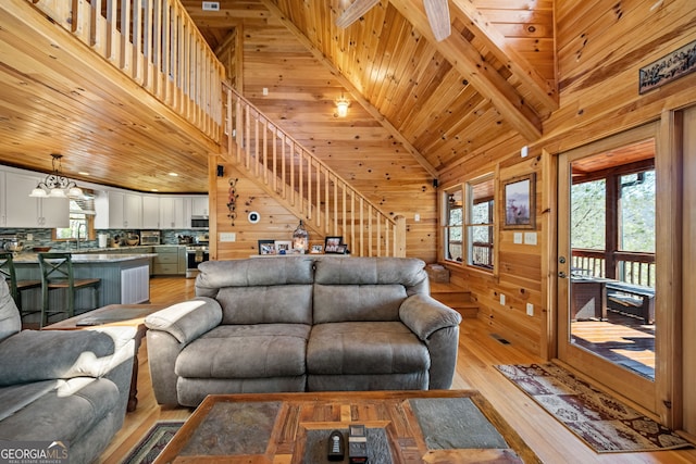 living room with wooden walls, wooden ceiling, stairway, light wood-type flooring, and high vaulted ceiling