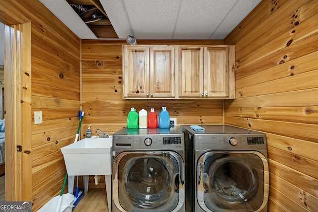 clothes washing area with wood walls, washing machine and dryer, and cabinet space