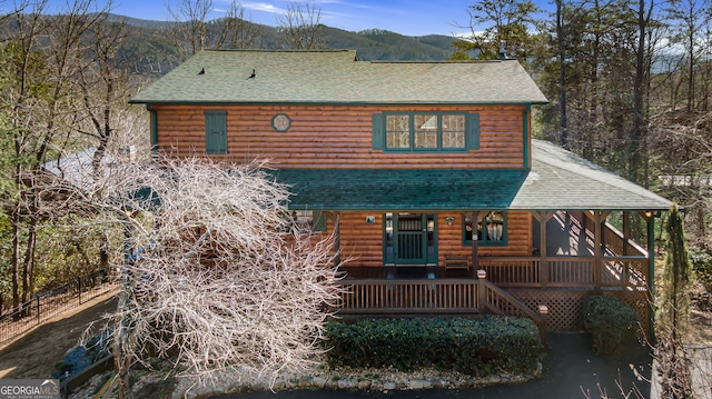 log cabin featuring covered porch, roof with shingles, a mountain view, and faux log siding