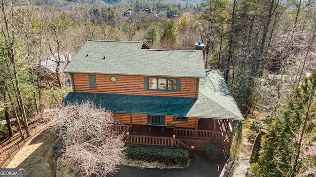 exterior space featuring a view of trees, roof with shingles, and faux log siding