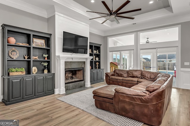 living area featuring a fireplace, ornamental molding, a ceiling fan, wainscoting, and light wood-type flooring