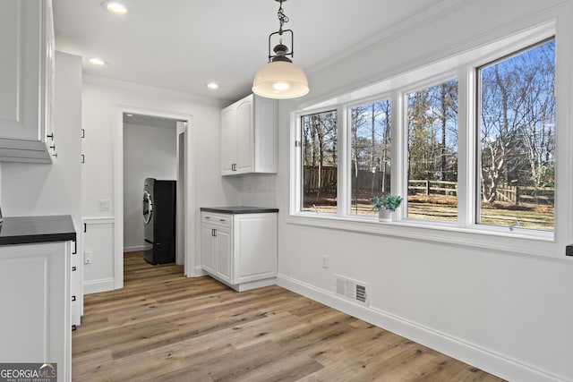 unfurnished dining area with light wood-type flooring, washer / dryer, plenty of natural light, and visible vents