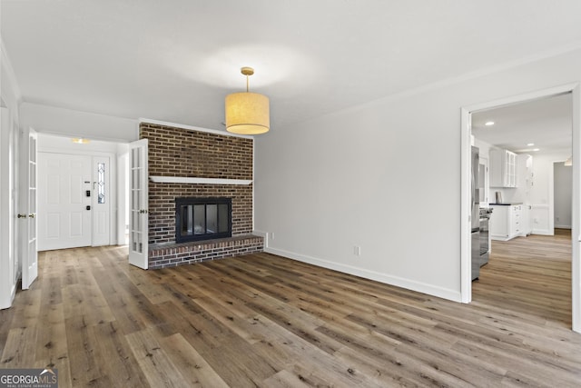 unfurnished living room with a brick fireplace, crown molding, baseboards, and wood finished floors