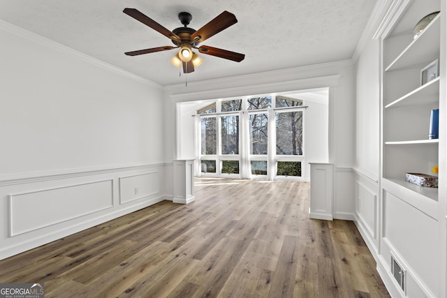 empty room with ceiling fan, a textured ceiling, ornamental molding, and wood finished floors