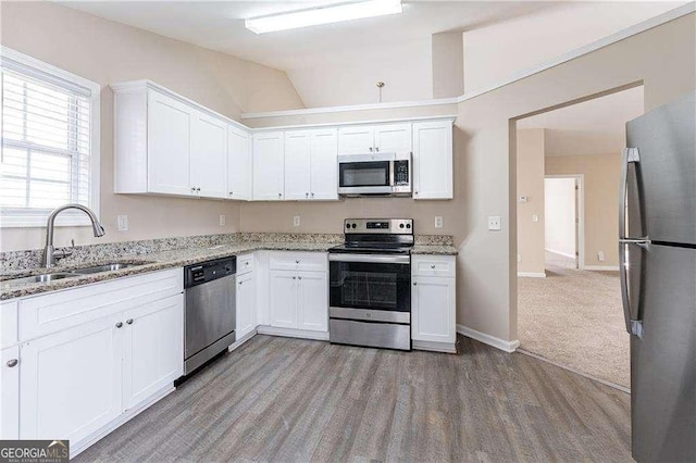 kitchen featuring light stone counters, a sink, white cabinets, appliances with stainless steel finishes, and light wood finished floors