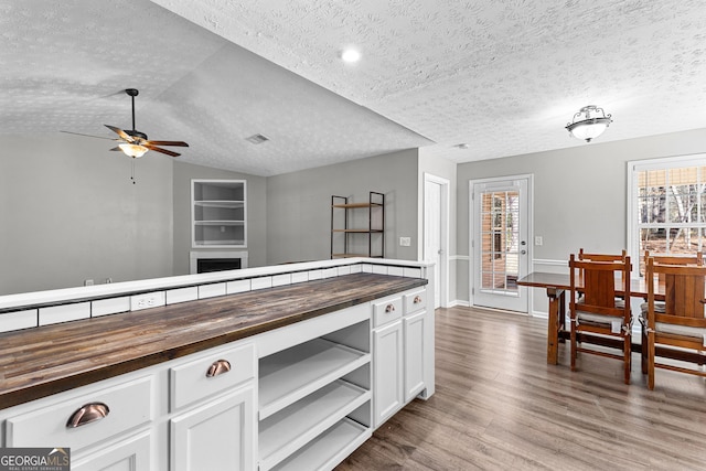 kitchen with a healthy amount of sunlight, wood finished floors, butcher block countertops, vaulted ceiling, and white cabinetry