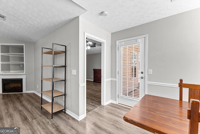 interior space featuring wood finished floors, baseboards, visible vents, a fireplace, and a textured ceiling