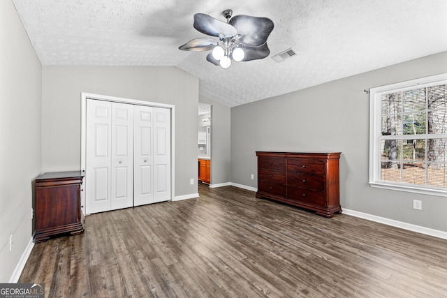 unfurnished bedroom featuring visible vents, vaulted ceiling, wood finished floors, a closet, and a textured ceiling