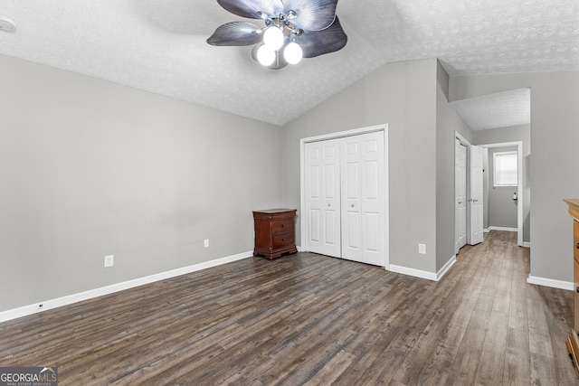 unfurnished bedroom featuring baseboards, a closet, lofted ceiling, dark wood-style floors, and a textured ceiling