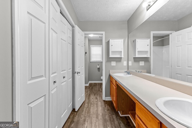 bathroom with a textured ceiling, toilet, wood finished floors, and a sink