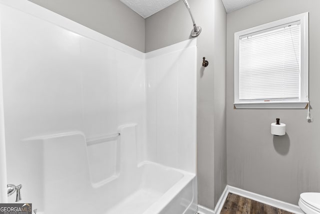 bathroom with baseboards, toilet, shower / bathing tub combination, wood finished floors, and a textured ceiling