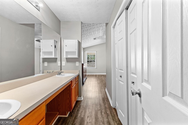 full bathroom with wood finished floors, baseboards, double vanity, a sink, and a textured ceiling