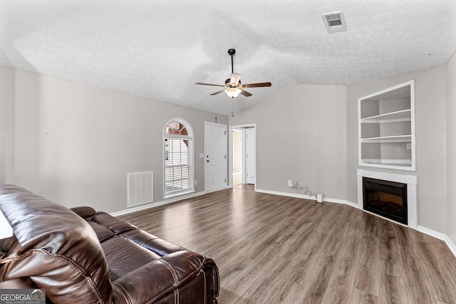 living room featuring visible vents, built in shelves, a fireplace, and wood finished floors