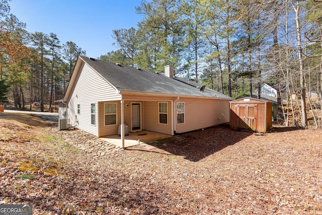 rear view of house featuring an outbuilding, a shed, cooling unit, a chimney, and a patio area