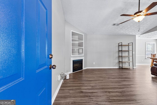 unfurnished living room featuring built in features, dark wood-style flooring, vaulted ceiling, a textured ceiling, and a glass covered fireplace