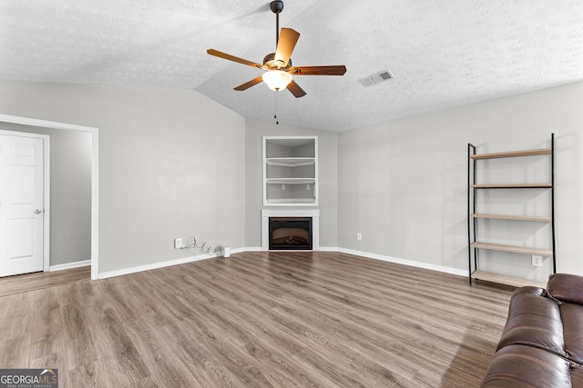 unfurnished living room with built in features, visible vents, wood finished floors, and a fireplace