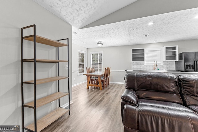 living area with vaulted ceiling, baseboards, light wood finished floors, and a textured ceiling