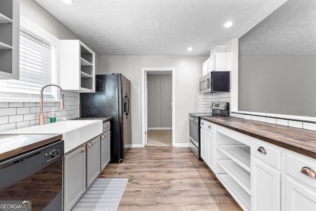 kitchen with open shelves, butcher block counters, light wood-style flooring, black appliances, and a sink